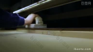 特写工人在车间内手持木板在固定水平电动带砂机上工作的木匠操作砂光机